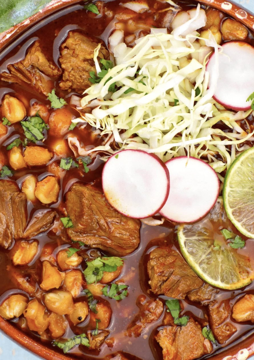 Stew with pork, vegetables in a thick tomato based sauce with slaw, radishes, and limes on top.